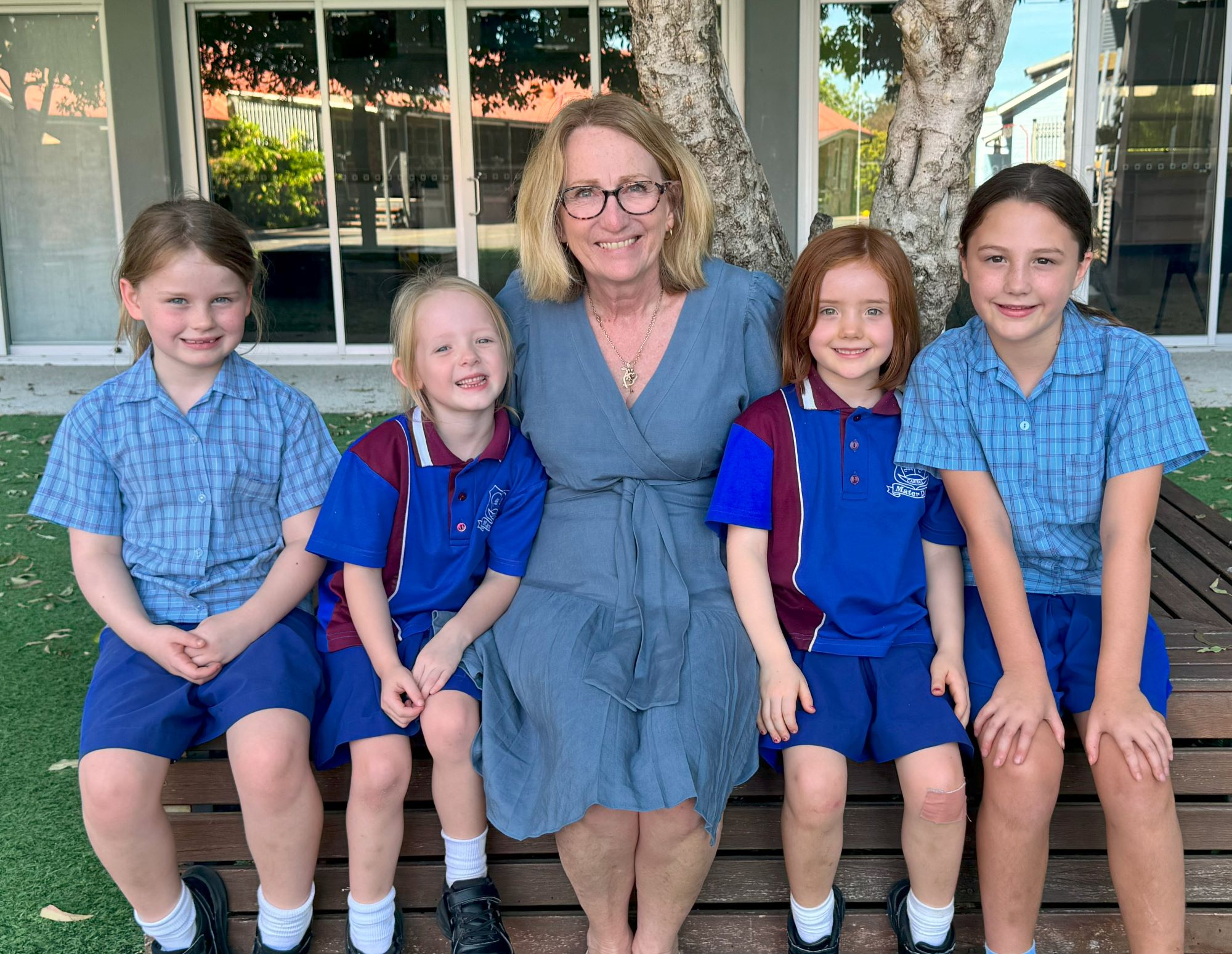 Adult staff member seated with young students on school grounds, highlighting caring relationships, pastoral support and a connected primary school community